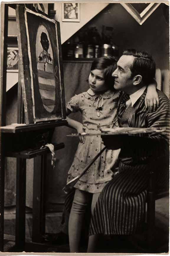 A man kneels in front of an easel with a paintbrush and palette in one hand. His other arm is wrapped around a girl, and both gaze at a painting he is evidently working on.