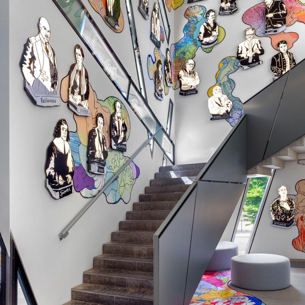 Colourful, comic-like busts of famous personalities on the walls of a staircase, seating below