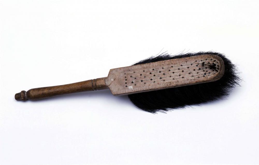 Fotografie: Ein Handfeger aus Holz mit stark abgenutzten schwarzen Borsten.