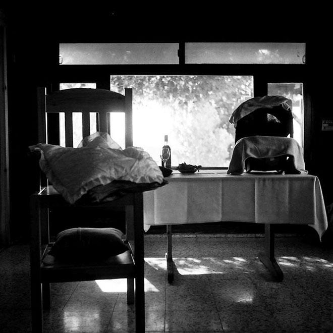 Schwarz-weiß Fotografie zeigt einen Tisch vor einem Fenster mit einer Babyschale, links davon ein Stuhl