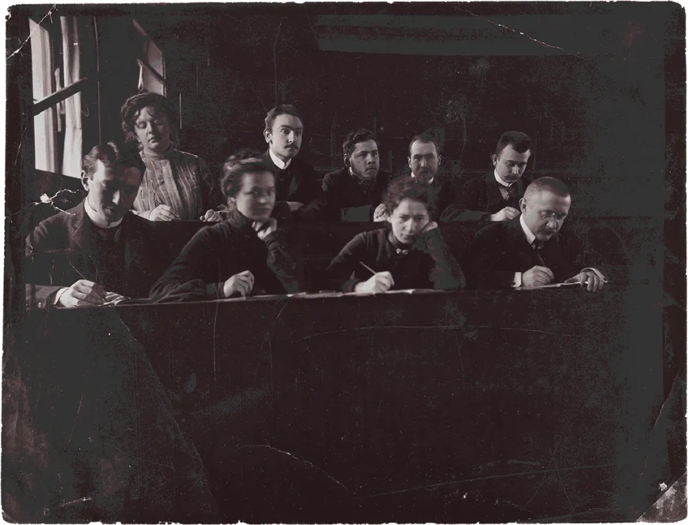 Historical black-and-white photograph of several writing students in a lecture hall.