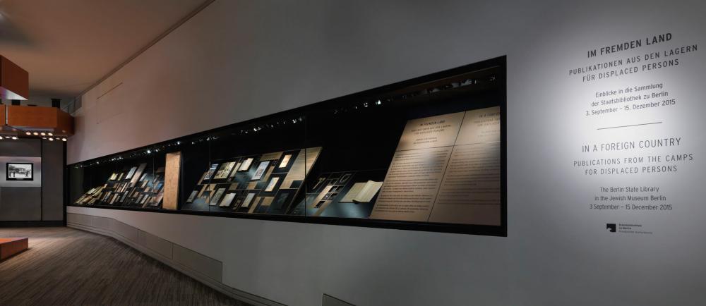A view of a long display case, in which different publications are exhibited, and at the end of the room is a monitor