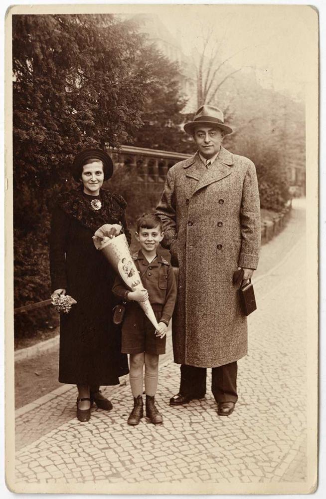 Photograph of the Zwilsky family in Monbijou Park, Berlin: The parents are wearing coats and hats. Klaus Zwilsky is wearing a shirt and shorts and holding a Schultüte
