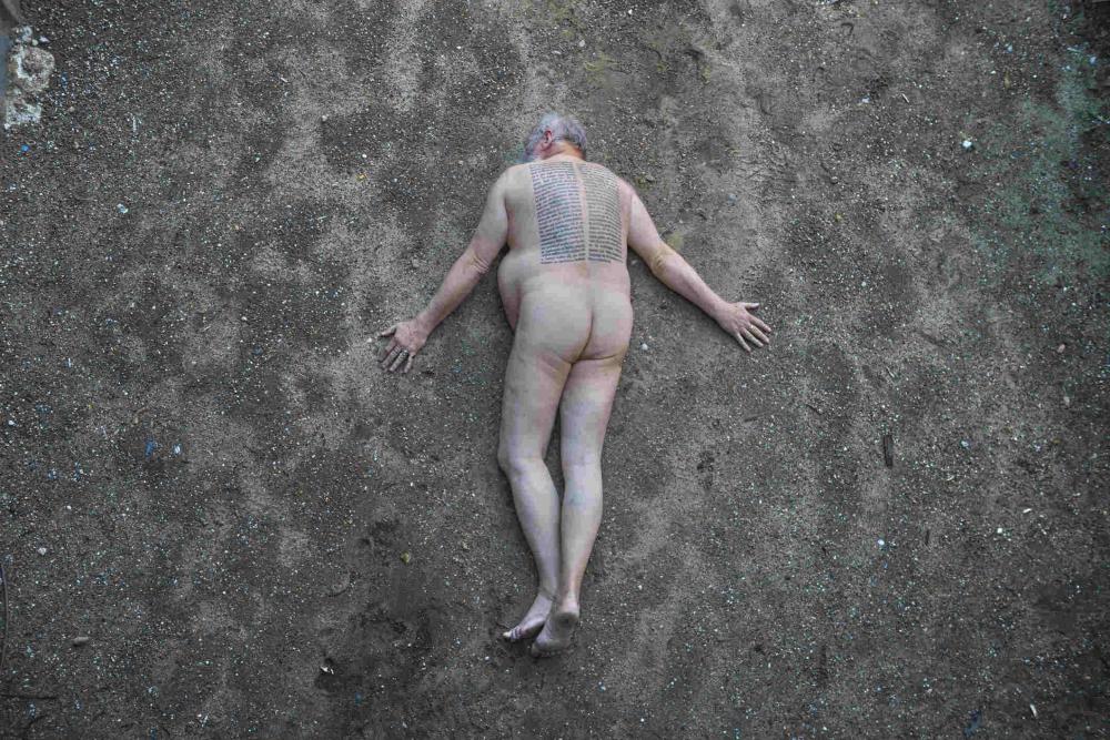 Nackter Mann mit tätowiertem Rücken liegt auf dunkler Erde