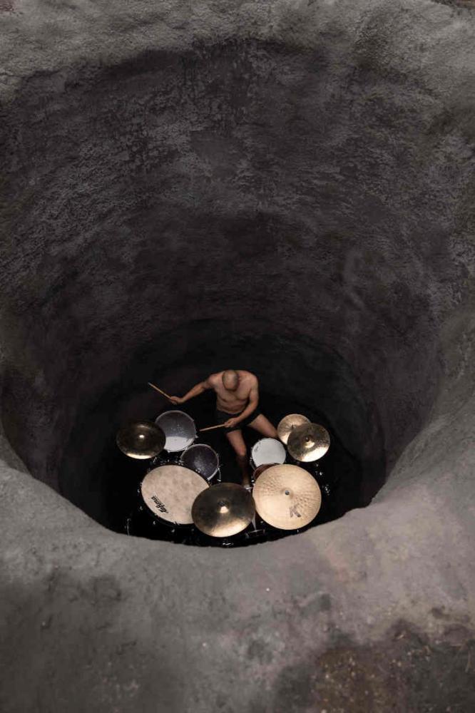 Man plays on a drum set in a hole in the ground