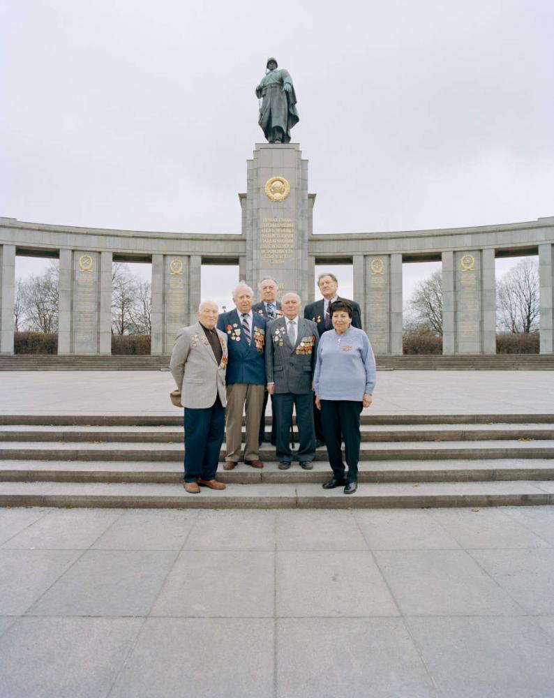 Alte Menschen stehen auf der Treppe vor einem Denkmal 