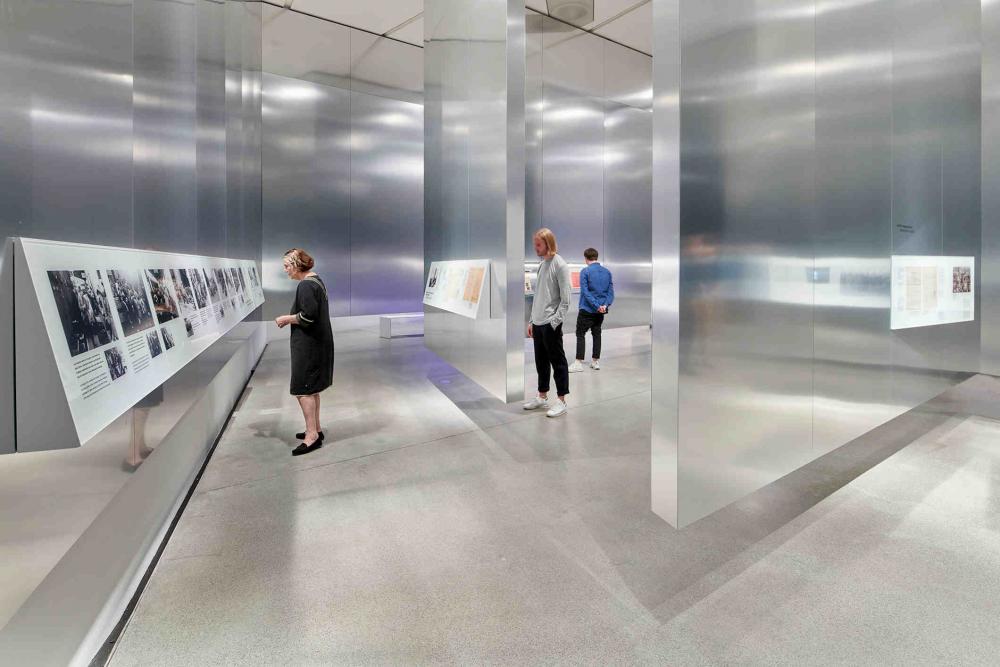 Metal walls hovering above the floor, 3 people reading texts attached to the walls