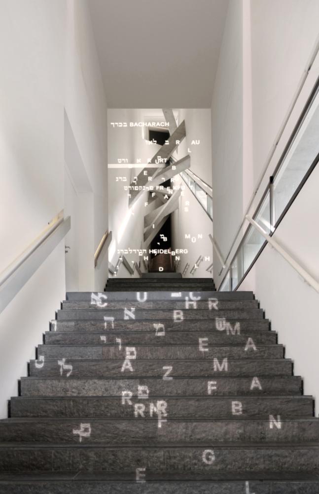Long staircase with projected Hebrew and Latin letters that form city names