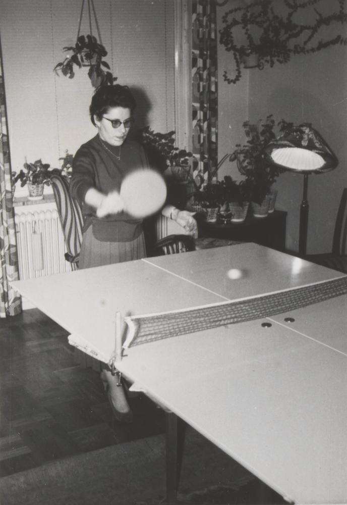 Eine Frau spielt Pingpong, im Hintergrund eine Stehlampe