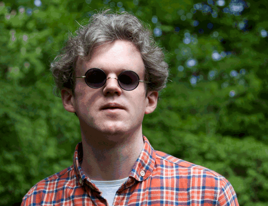 Porträt von Jonas Hauer mit kariertem Hemd, Sonnenbrille vor einem Baum