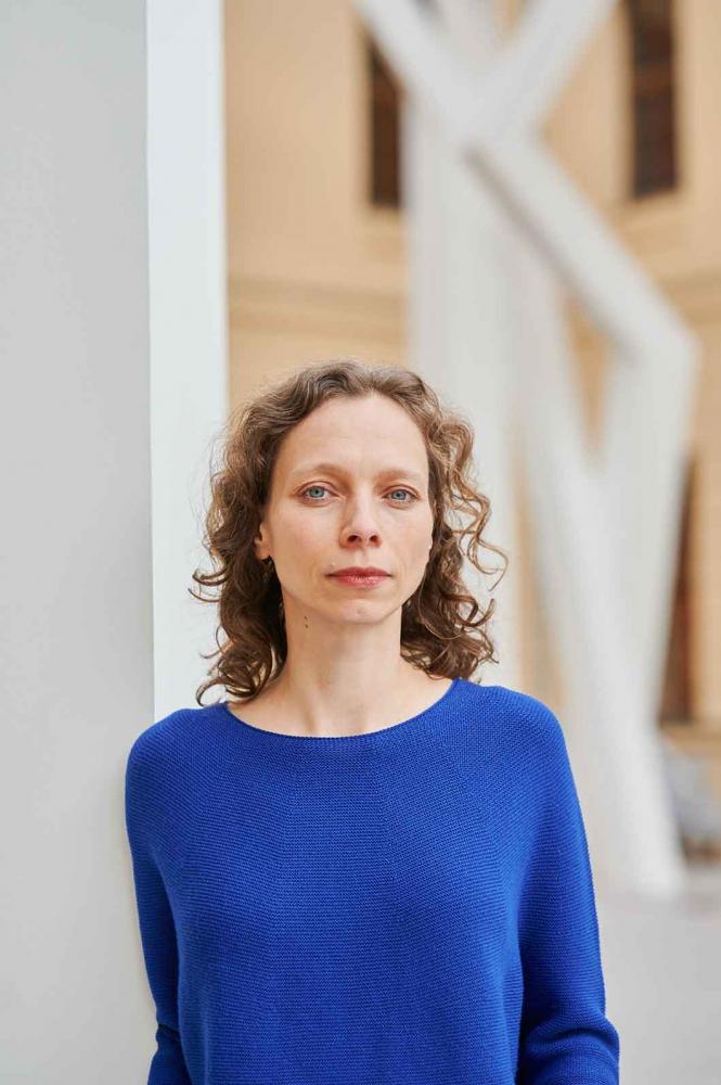 Portrait photo of a woman wearing a bright blue jumper: she looks directly into the camera. 