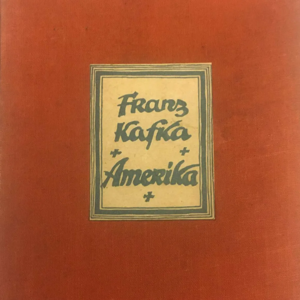 Ausschnitt aus einem roten Buchcover mit aufgeklebtem, gerahmtem Etikett mit der Aufschrift: „Franz Kafka, Amerika“.