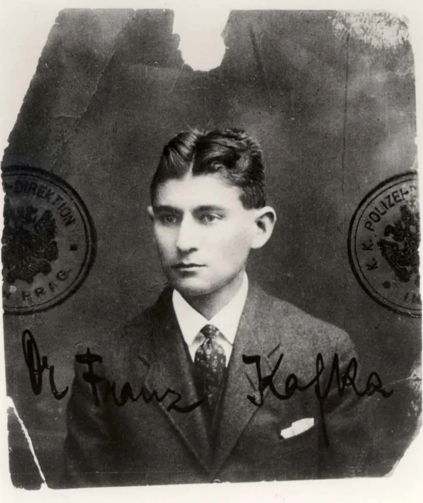 Black and white passport photo of a young man with a gelled middle parting, stamp and signature on the photo: Dr. Franz Kafka.