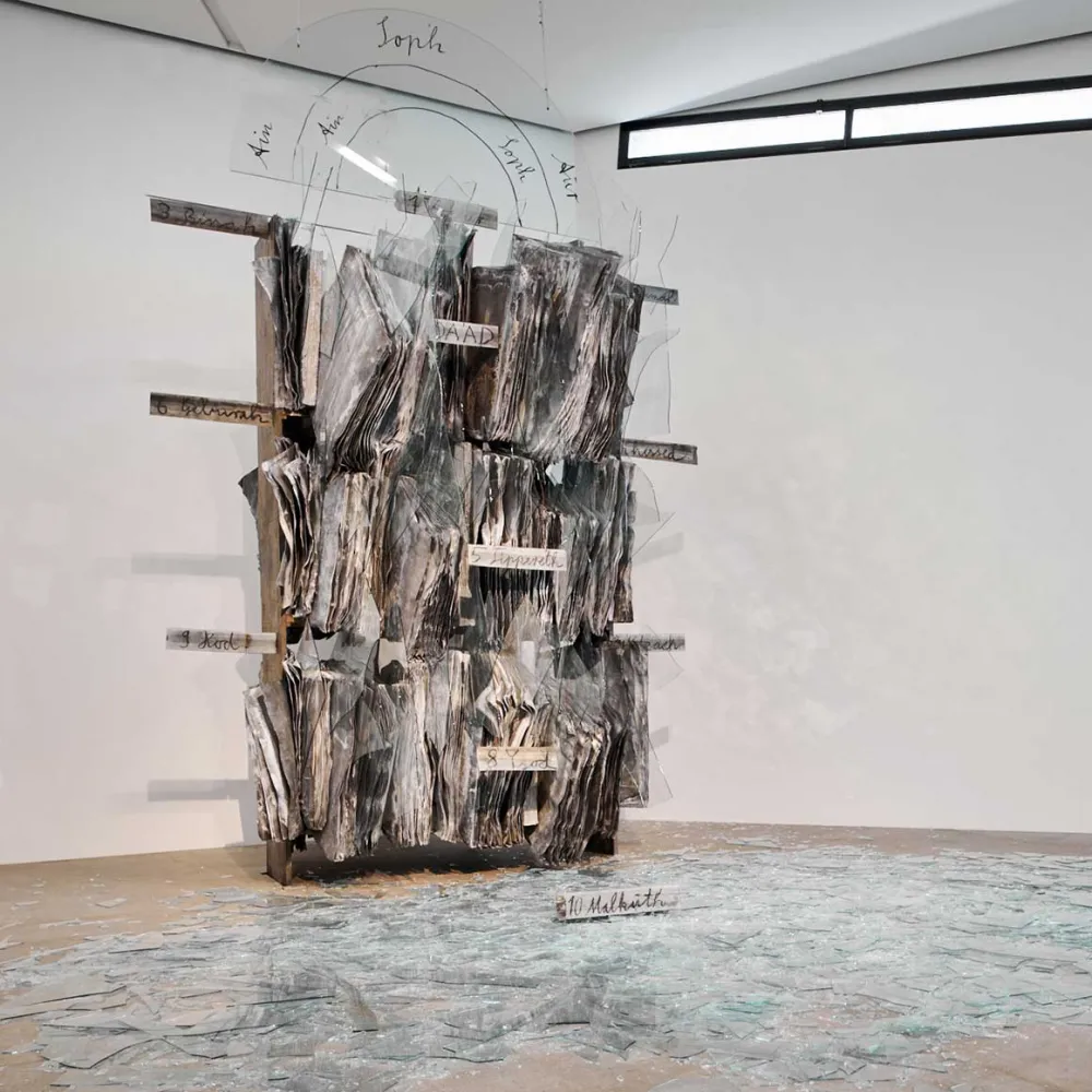 Sculpture of a library made of lead with inserted glass fragments, above a semicircle with the name of the infinite god
