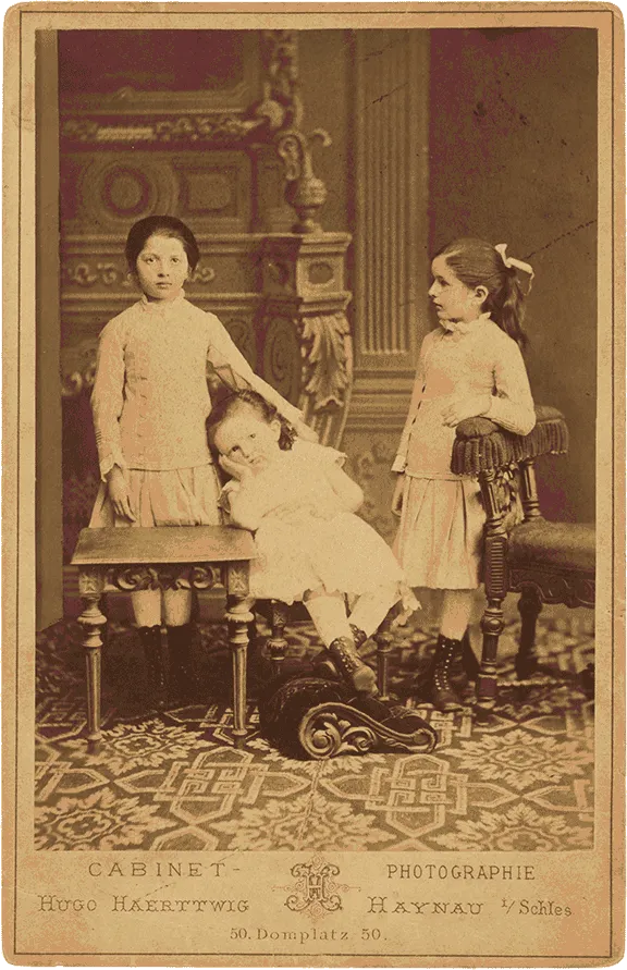 Historical black and white photograph of three children in white dresses.