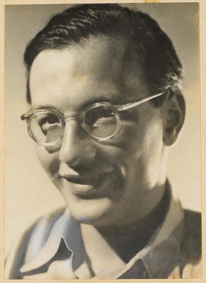 Black-and-white photograph of a young man with eyeglasses, smiling into the camera (half profile)