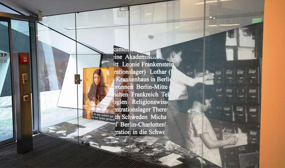 Display case with oversized photos of people, archive boxes and texts. 