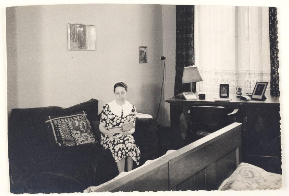 Schwarz-Weiß-Fotografie: eine Frau sitzt mit einem aufgeschlagenen Buch in den Händen auf einem Sofa uns schaut ins Leere
