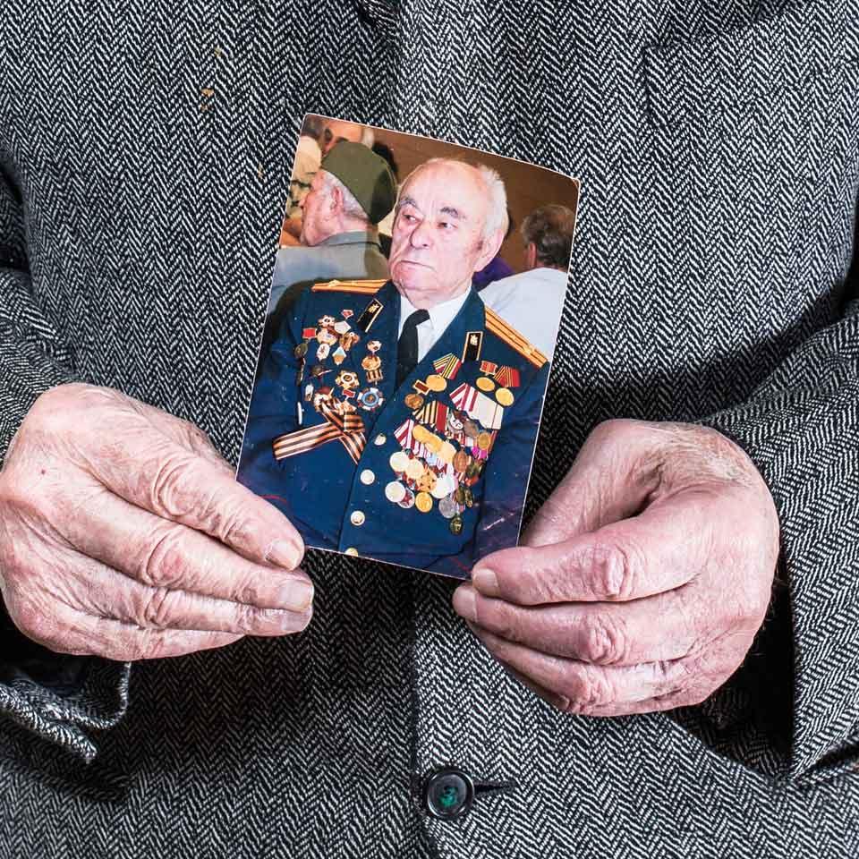Hände halten das Foto eines Mannes, der eine mit vielen Bändern und Medaillen geschmückte Uniform trägt.