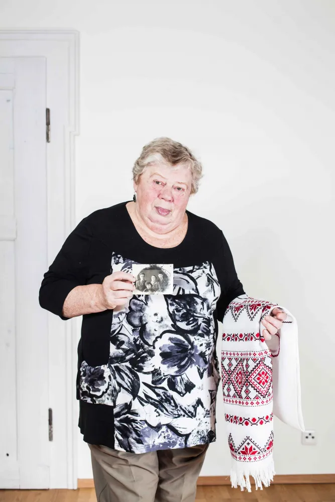 An elderly lady holding an embroidered wedding scarf and a black and white photograph in her hands
