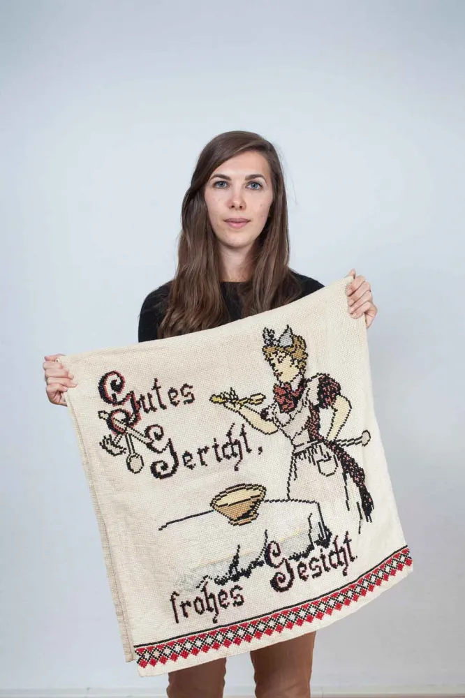 A young woman with long hair holding an embroidered tapestry in her hands