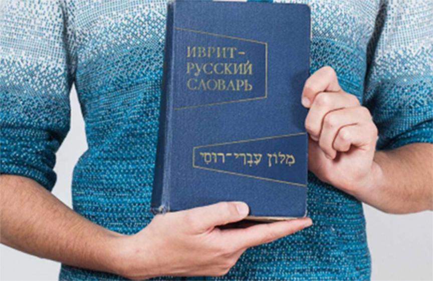 Hände halten ein Buch mit russischer und hebräischer Schrift darauf