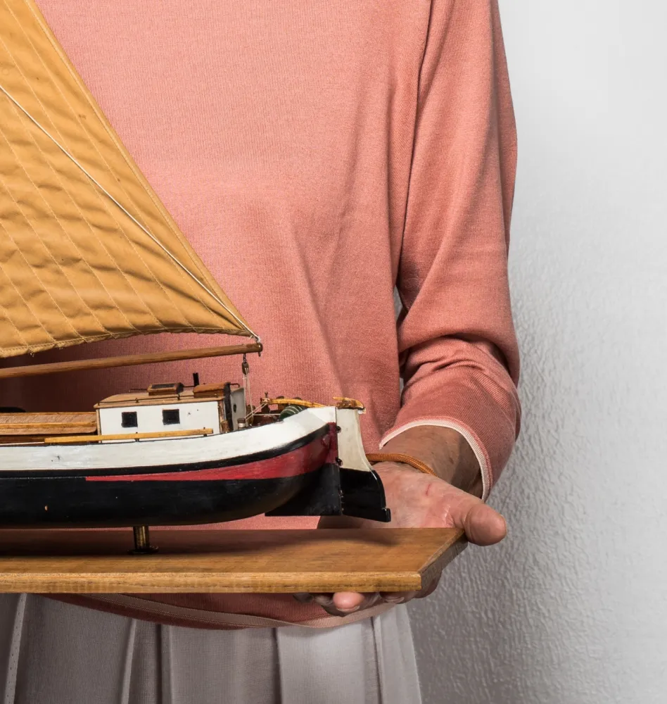 Hands holding a wooden board with a model ship on it.