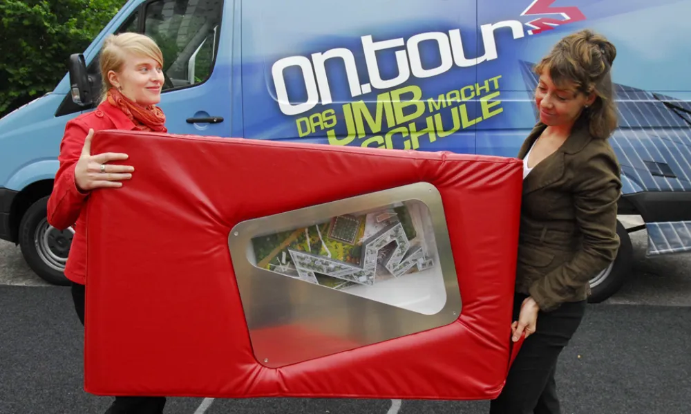 Two on.tour employees carry a red cube with a model of the Libeskind building from the Jewish Museum.
