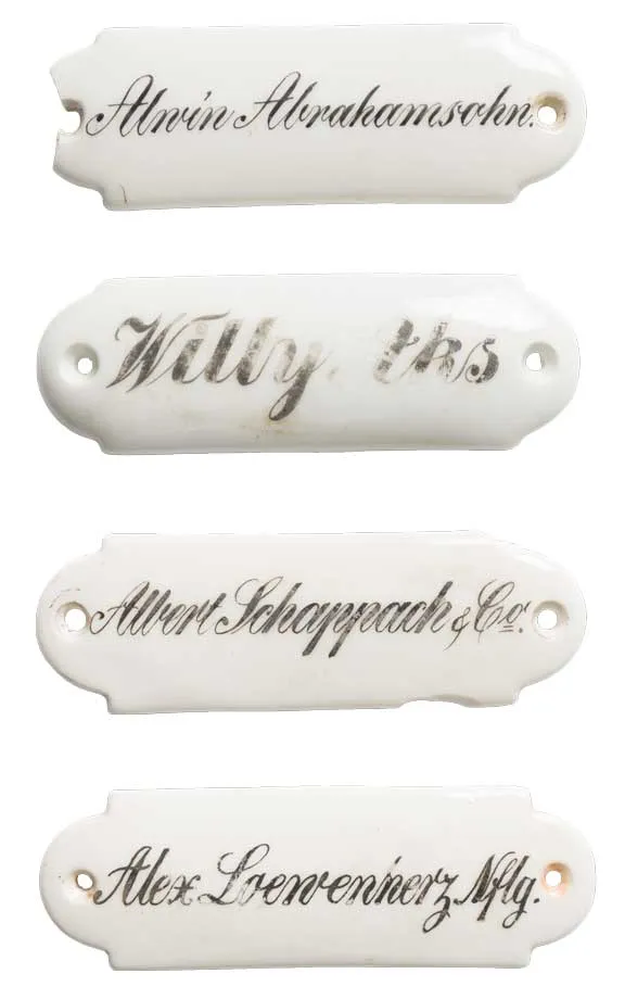 Four white porcelain signs one below the other with the names Abrahamsohn, Aks, Schappach and Loewenherz written in cursive.