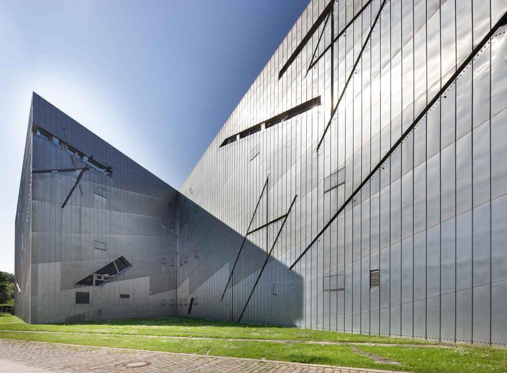 New building made of metal elements behind a green field.