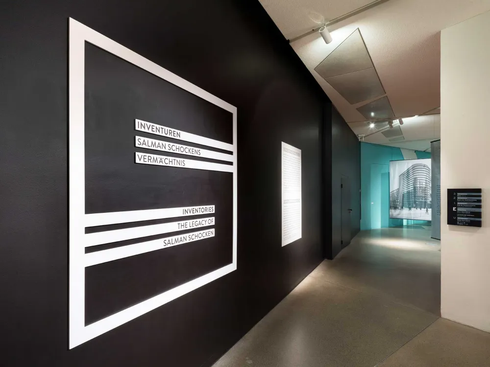 View into an elongated exhibition room, on the long black wall to the left is the large S-shaped Schocken logo with the inscription: Inventories. The legacy of Salman Schocken.