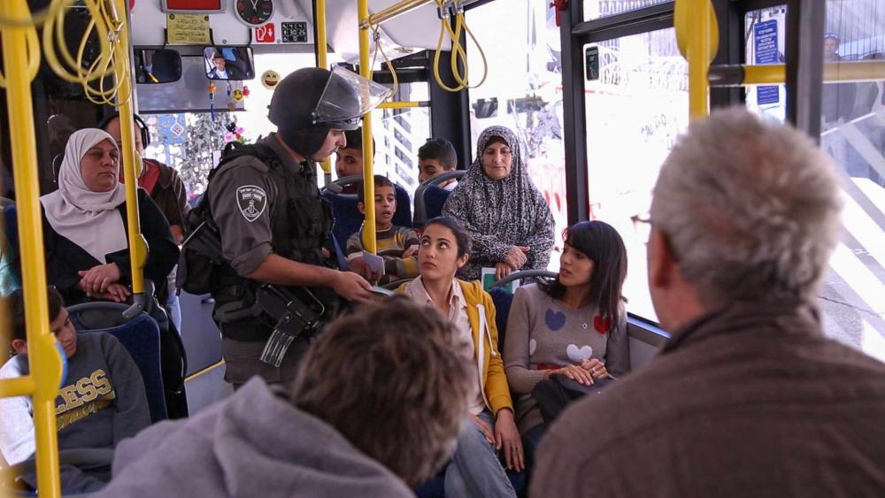 An armed soldier checks civilians' identification on a bus