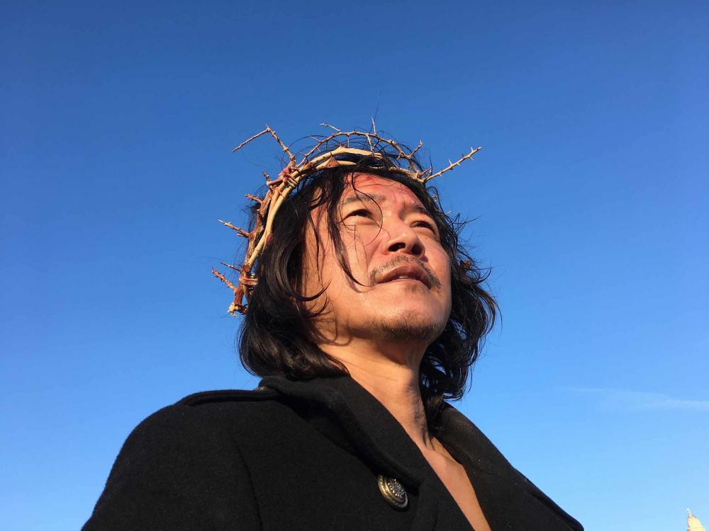 Portrait photo of a man with a crown of thorns, taken from below, before a bright blue sky