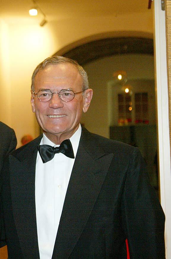 Man with glasses, jacket and black bow tie smiles at camera.