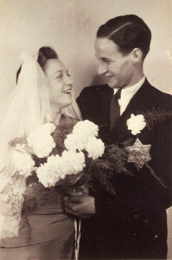 Black and white photograph of a couple with a bouquet of flowers and a veil,  a yellow badge on his jacket.