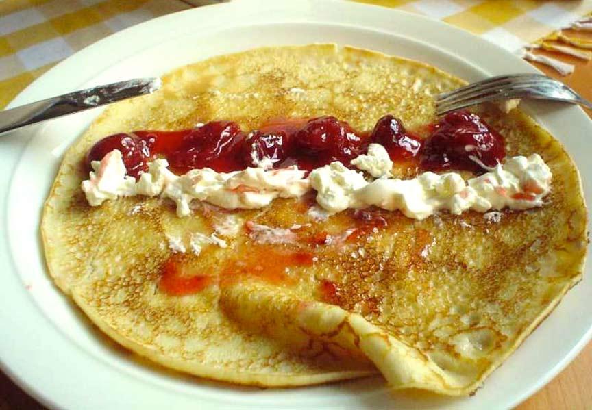 Geöffneter Eierpfannekuchen mit eingemachten Kirschen und Sahne