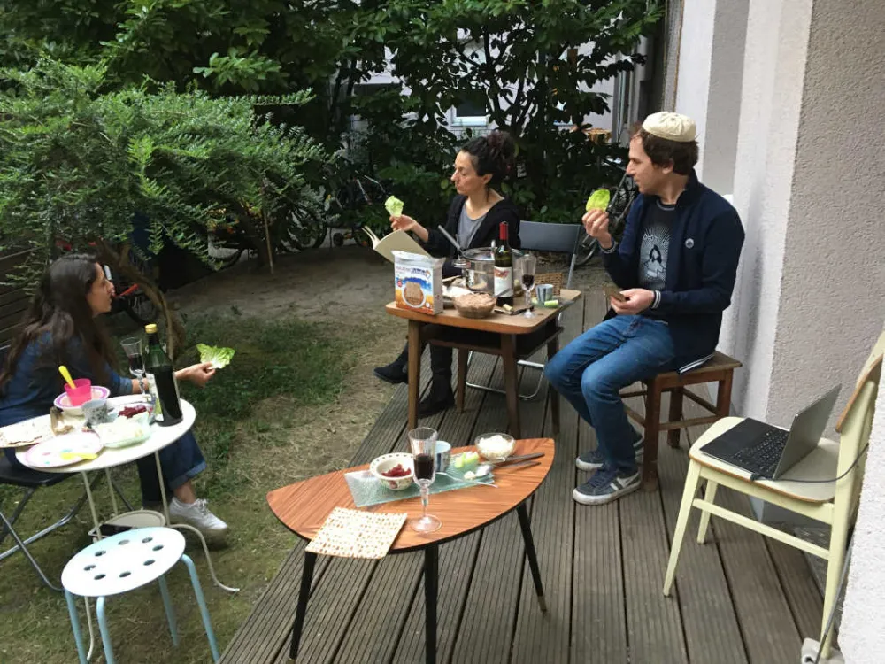 On a terrace three people sit at a distance from each other and eat.