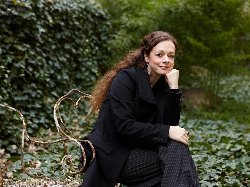 Portrait of Shelly Kupferberg sitting in a garden, smiling, chin resting on hand