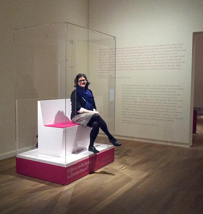A woman sitting on a bench in a vitreous showcase open at the front
