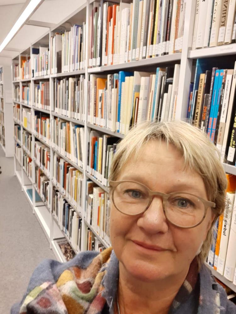 Selfie by Ulrike Sonnemann in front of a bookshelf in the library