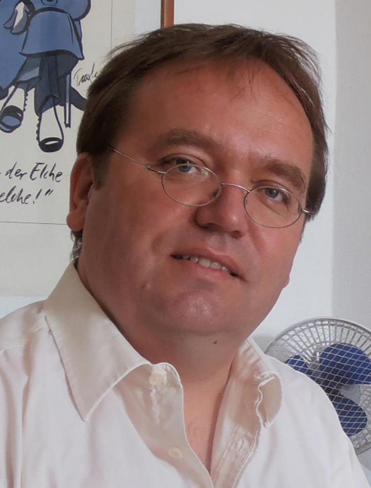 Portrait of Stefan Vogt in white shirt, with glasses. He looks neutrally into the camera.