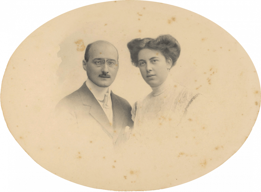 The oval photo shows a man on the left and a woman on the right, each as a breast portrait. He is wearing a suit with a pocket square and a monocle, she is wearing a white, high-necked top and an updo.