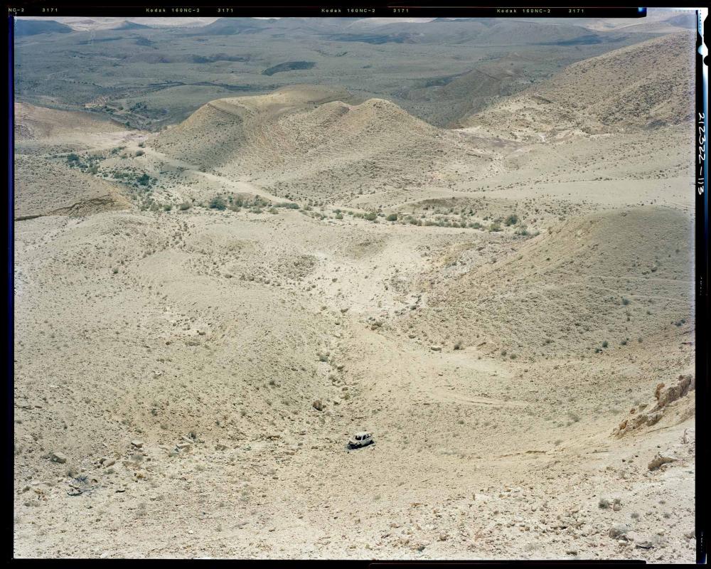 Blick von oben auf hügelige Wüstenlandschaft mit einzelnem Auto