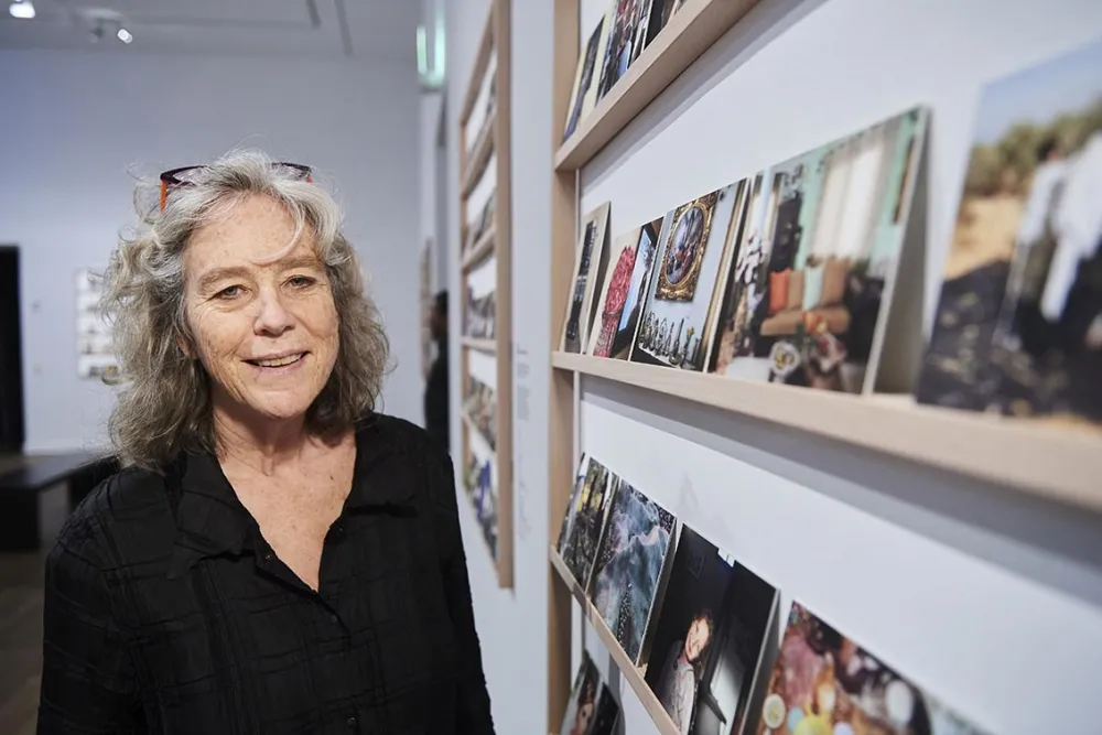 Wendy Ewald stands next to a shelf with photographs