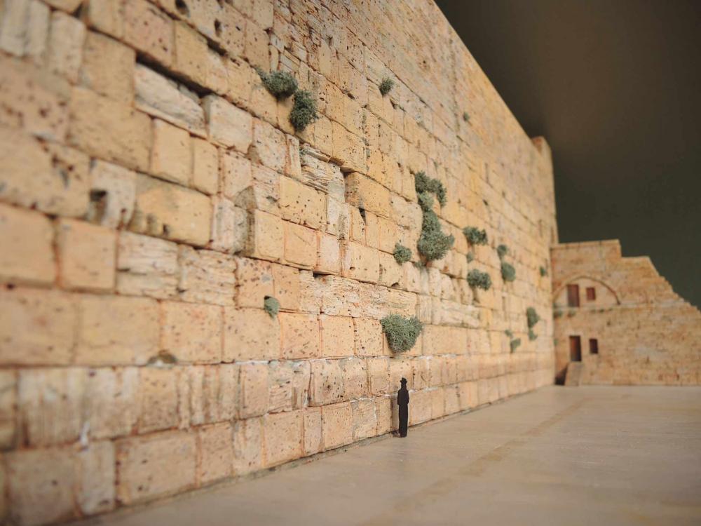  Das Foto zeigt eine Figur, die vor der Klagemauer steht und ist von schräg unten fotografiert.