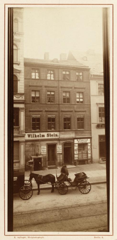 Yellowed black and white photograph of a residence with horse-drawn carriage in front of the door and a sign above the door reading: Wilhelm Stein