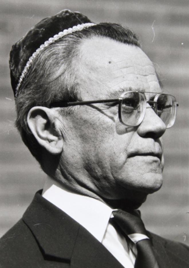 Black-and-white portrait of a man in semi-profile waring a kippah, glasses, a suit, and a tie