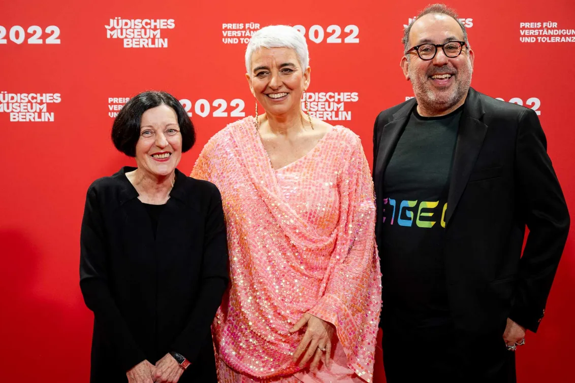 Hetty Berg in a red sequined dress between Herta Müller and Barrie Kosky, both in black, all laughing into the camera.