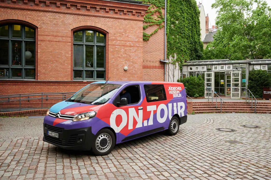 Red and purple van with the logo on.tour parked in a school yard.