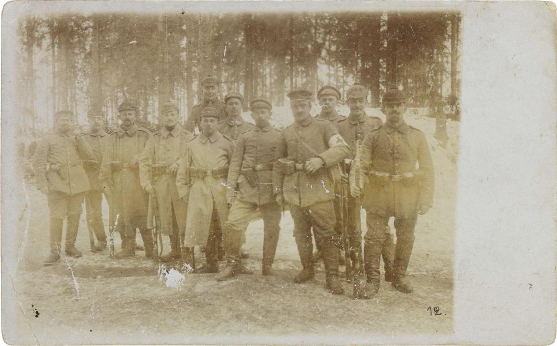 Schwarz-weiß-Foto: 12 uniformierte Soldaten, in einem verschneiten Nadelwald stehend